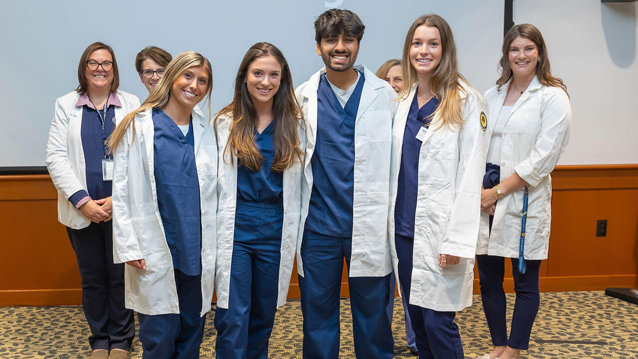 four nursing students wear white coats to pose for a photo