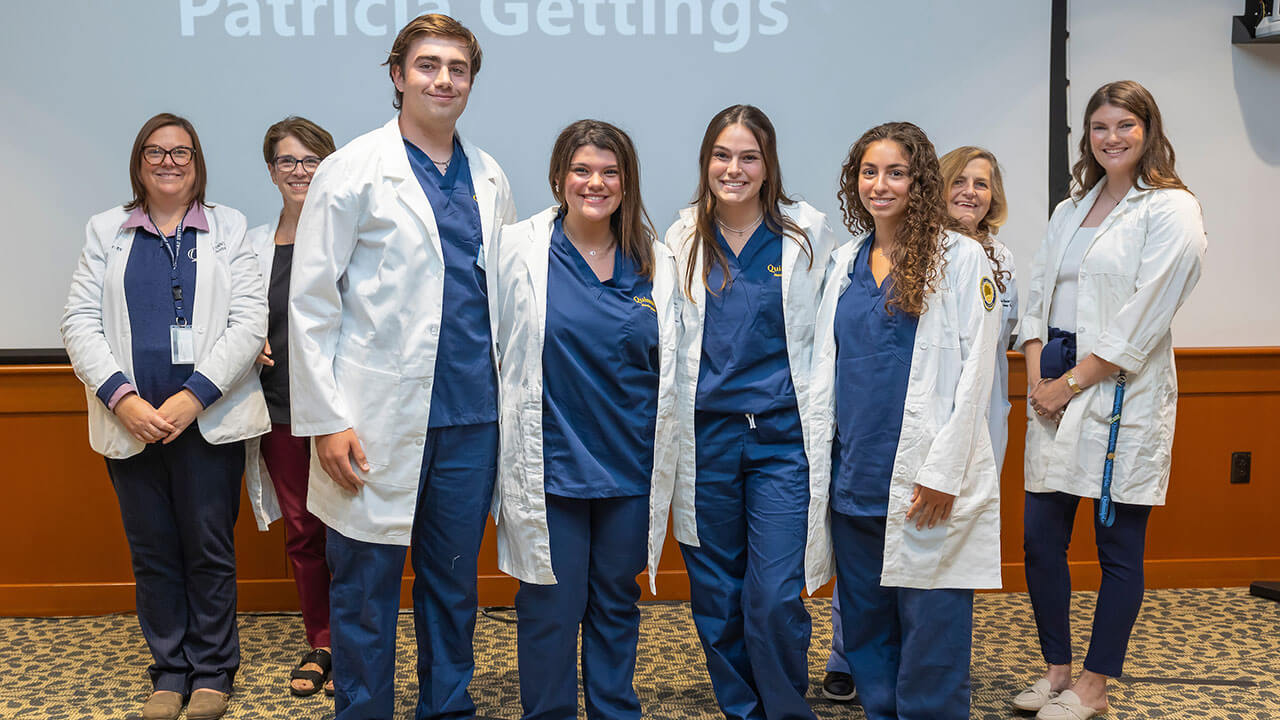 four nursing students and their advisors pose wearing white coats