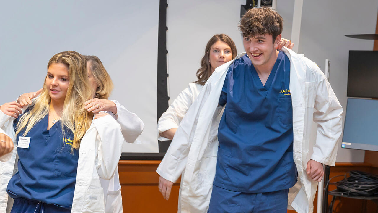 two nursing students have their white coats placed on them by their advisors