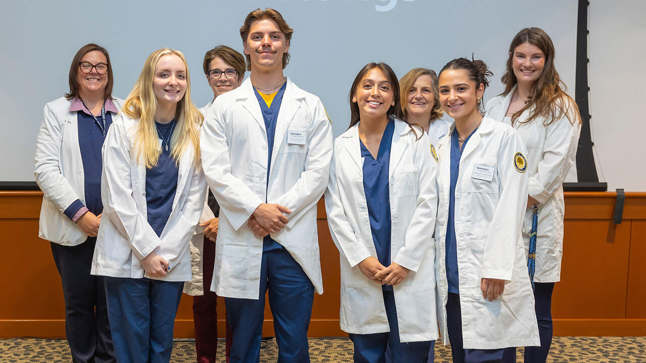 four nursing students in white coats pose smiling