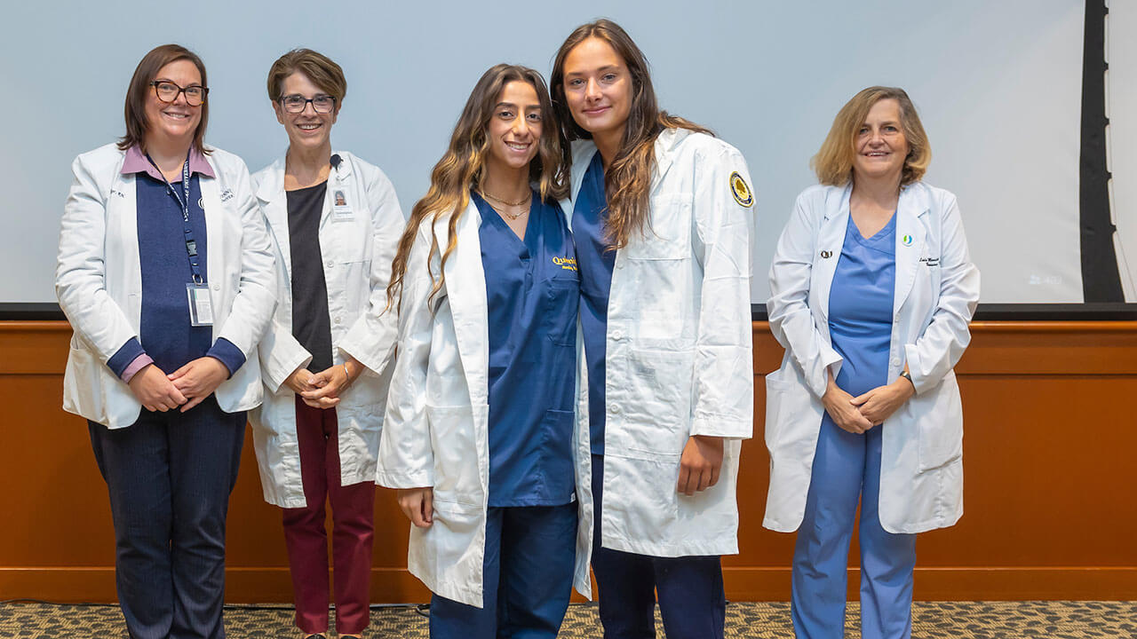 two nursing students smile in front of their advisors with their new white coats