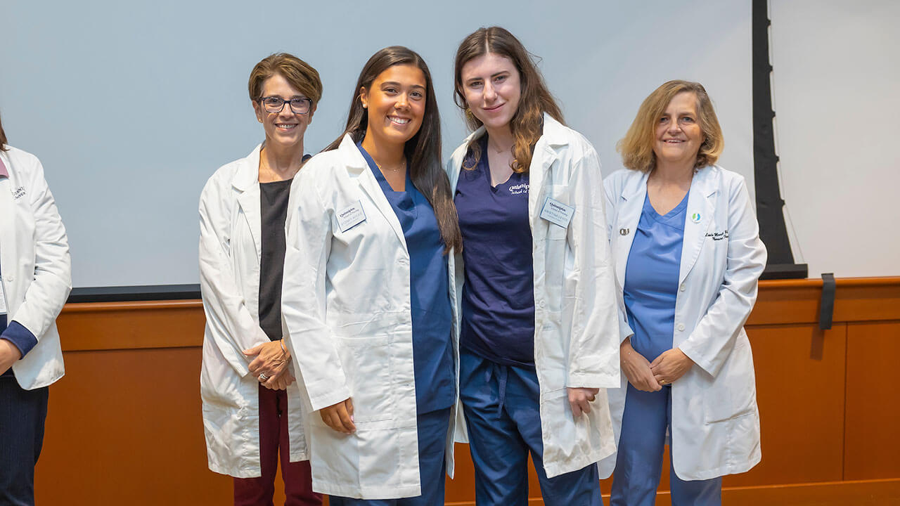 two nursing students in white coats pose in front of their advisors