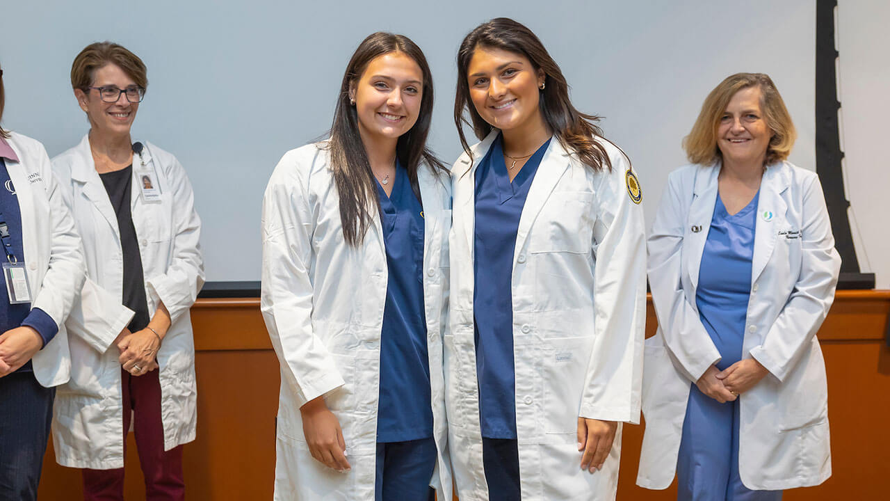 two nursing students show off their new white coats and pose for a photo