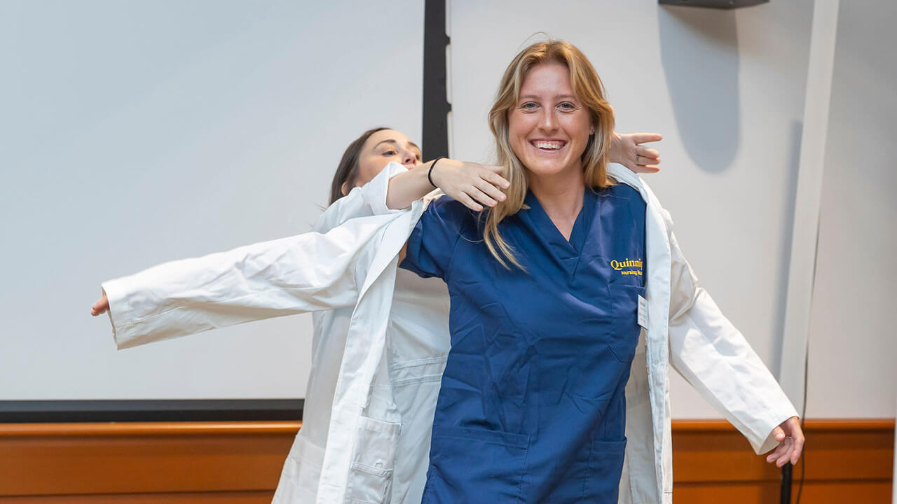 nursing student smiles widely while putting on her brand new white coat