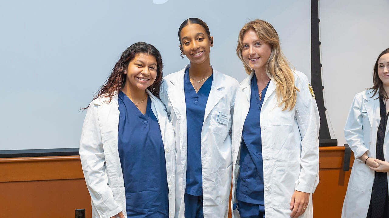 three nursing students pose together with their new white coats