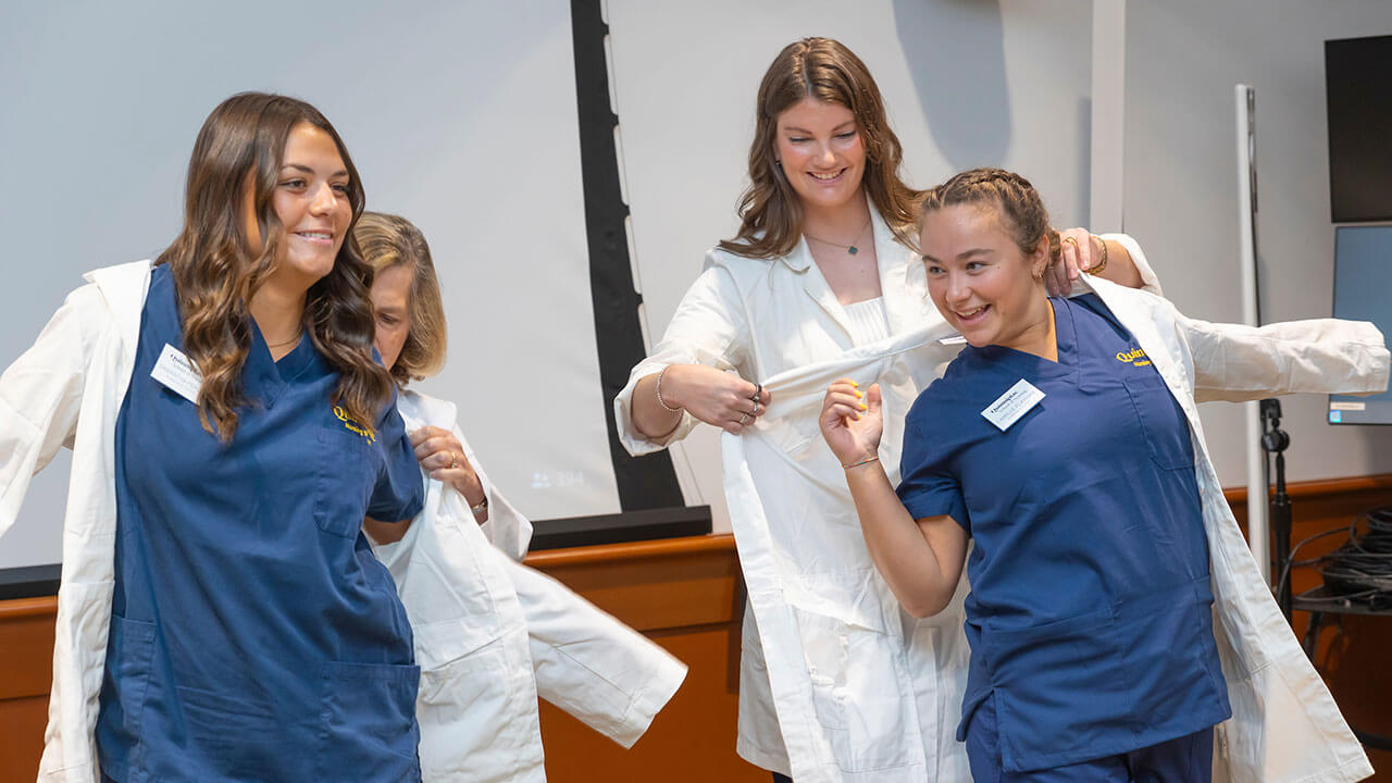 two nursing students have their white coats placed on them by their advisors