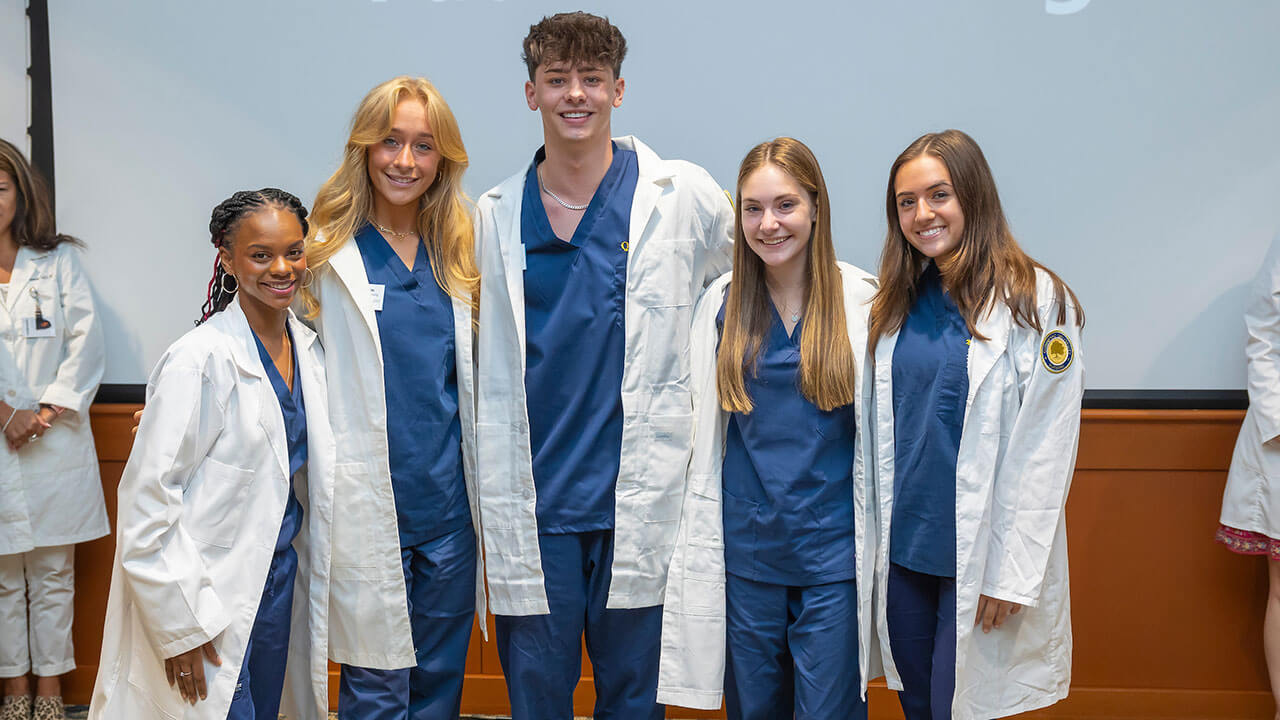 five nursing students pose smiling together as they wear their new white coats