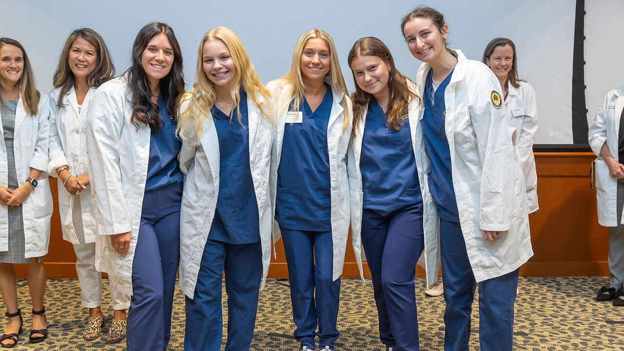 five nursing students pose excitedly together with their new white coats