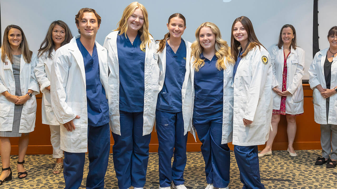 five nursing students smile together in their new white coats
