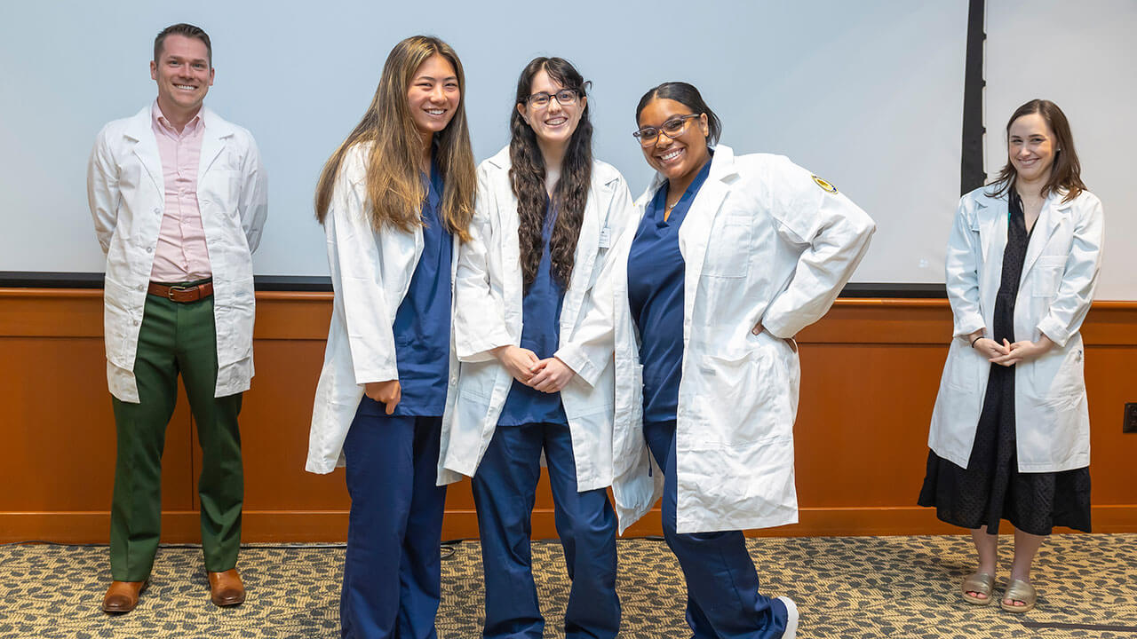 three nursing students pose together wearing their white coats