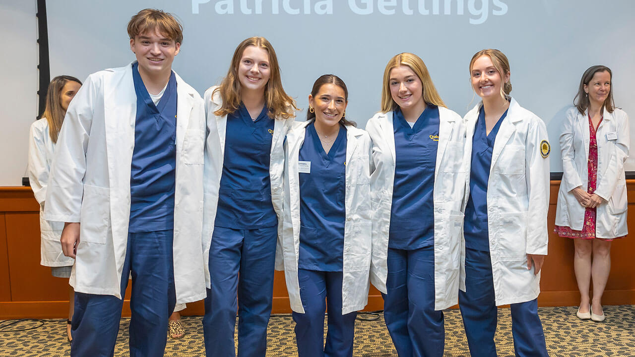 five nursing students smile together wearing their new white coats