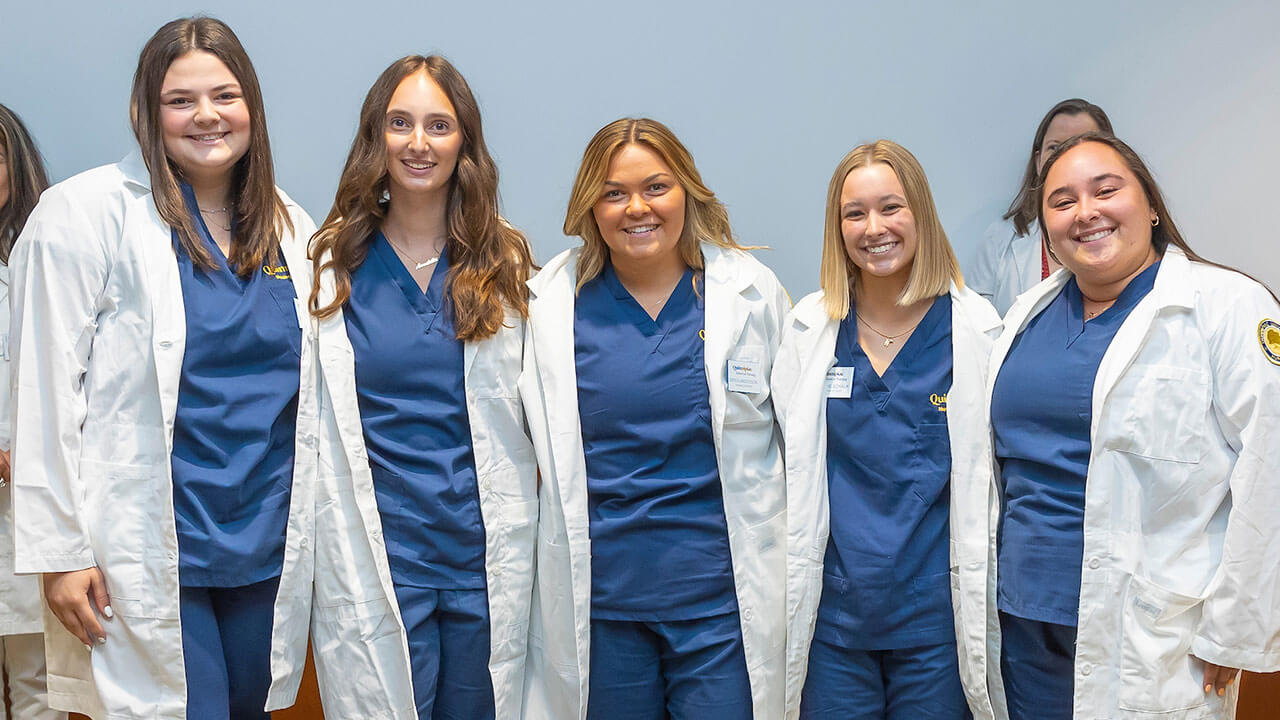 five nursing students smile for a photo wearing their white coats