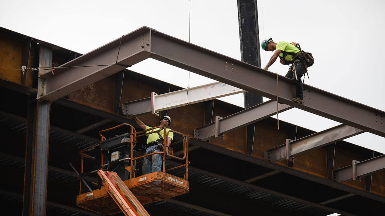 Construction workers in green shirts working on tall beams