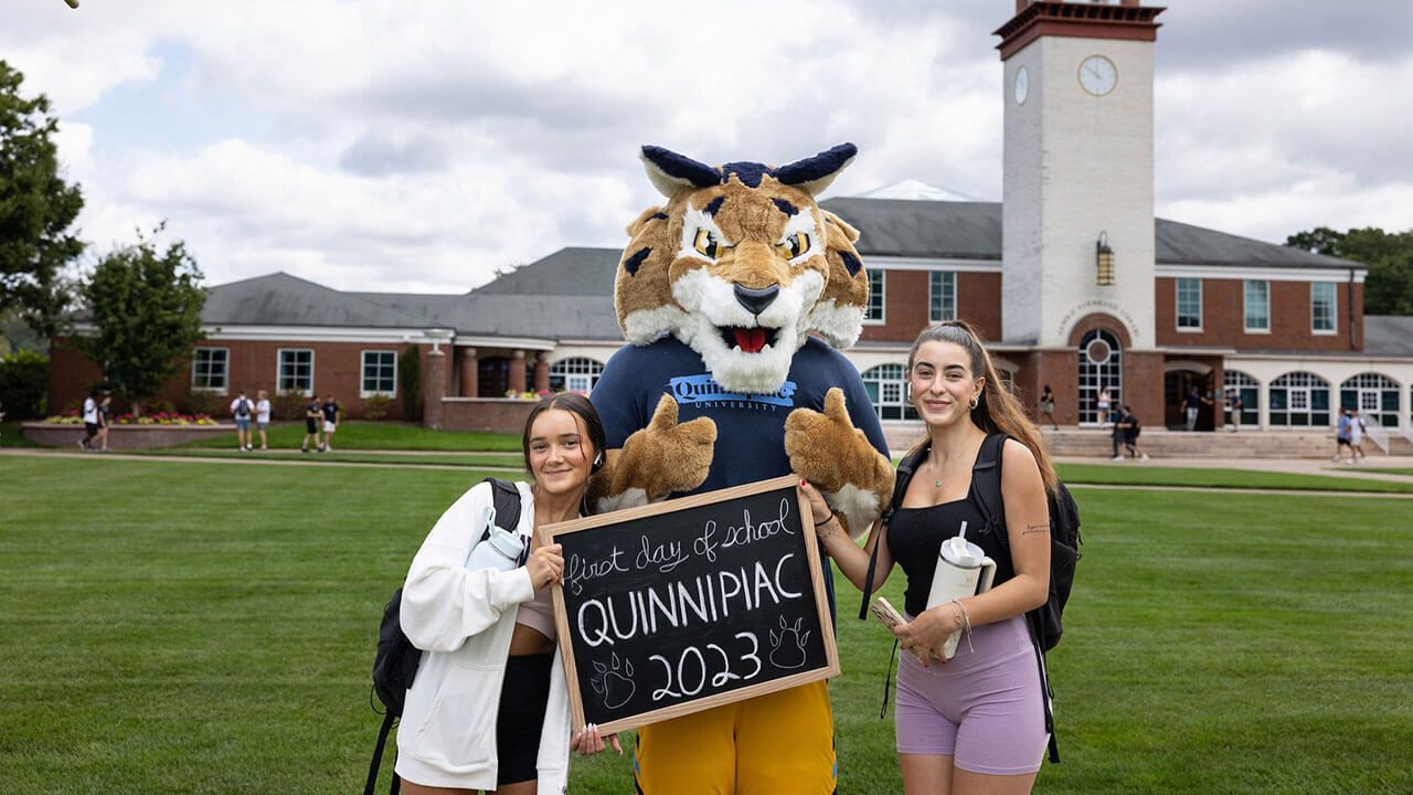Two students take a photo with Boomer in front of the clocktower