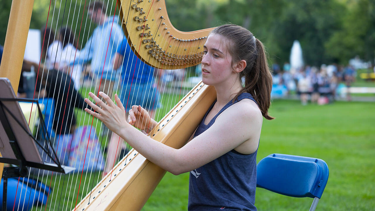 A student plays the harp on the Quad