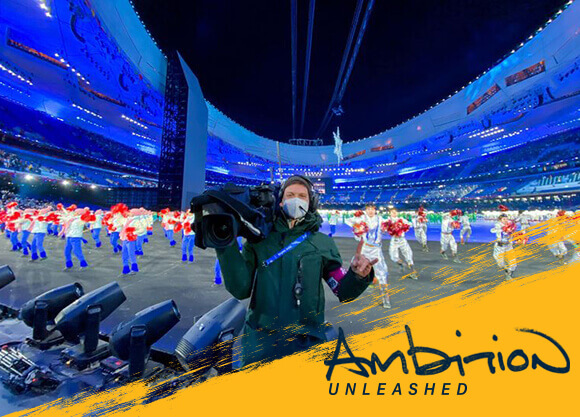 Ambition Unleashed: Matt Andrew holds his camera and smiles in the Olympic stadium in Beijing