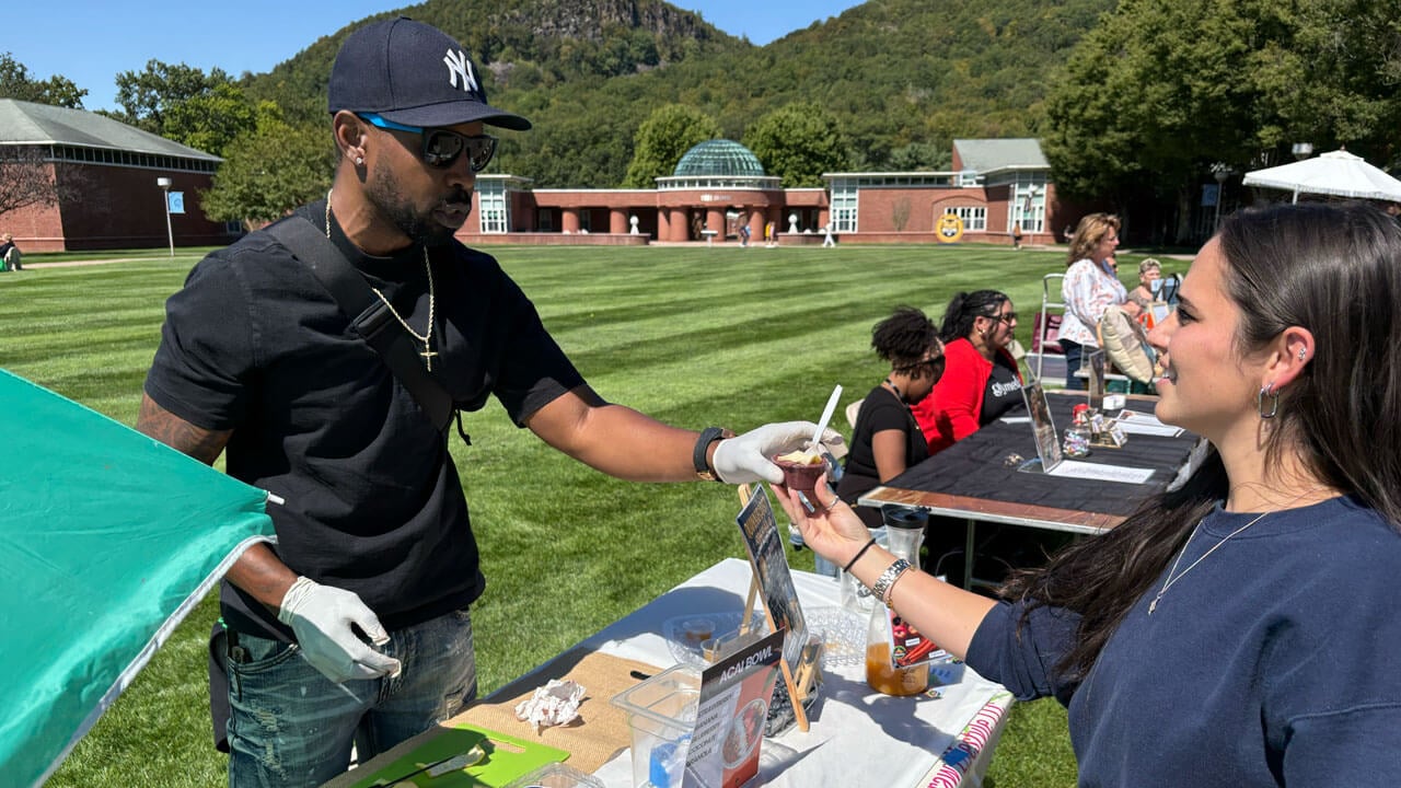 Entrepreneur hands student a sample from their business stand