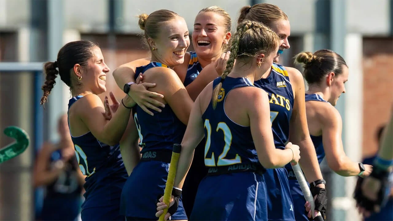 Six field hockey players gather around each other; two of them hug.