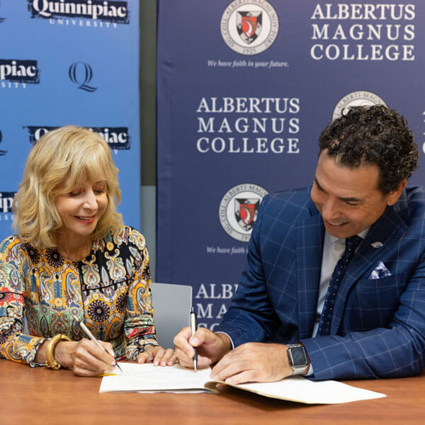 Judy Olian and Albertus Magnus College President Marc Camille sign a document