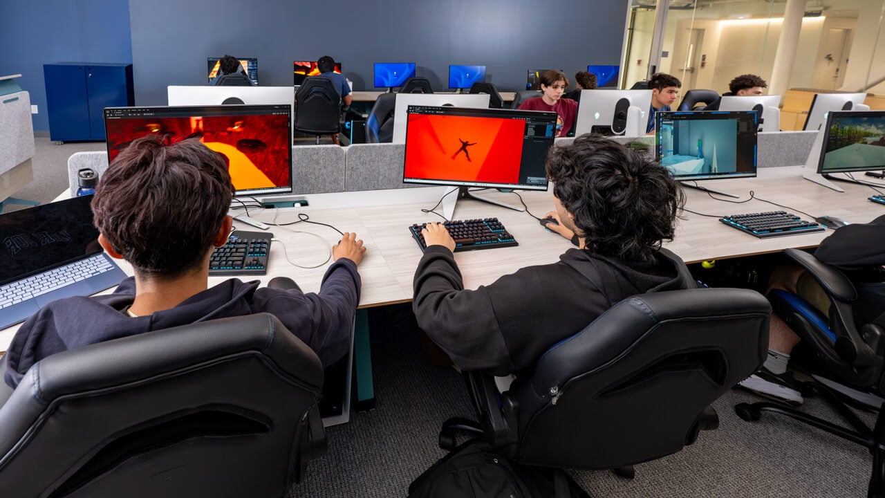 A shot from behind of students working on monitors with colorful animations.