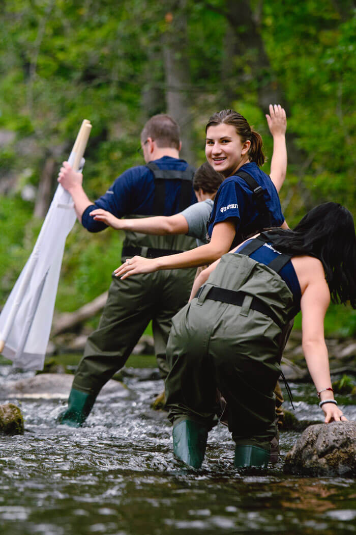 Students wade through a river while conducting an experiment.