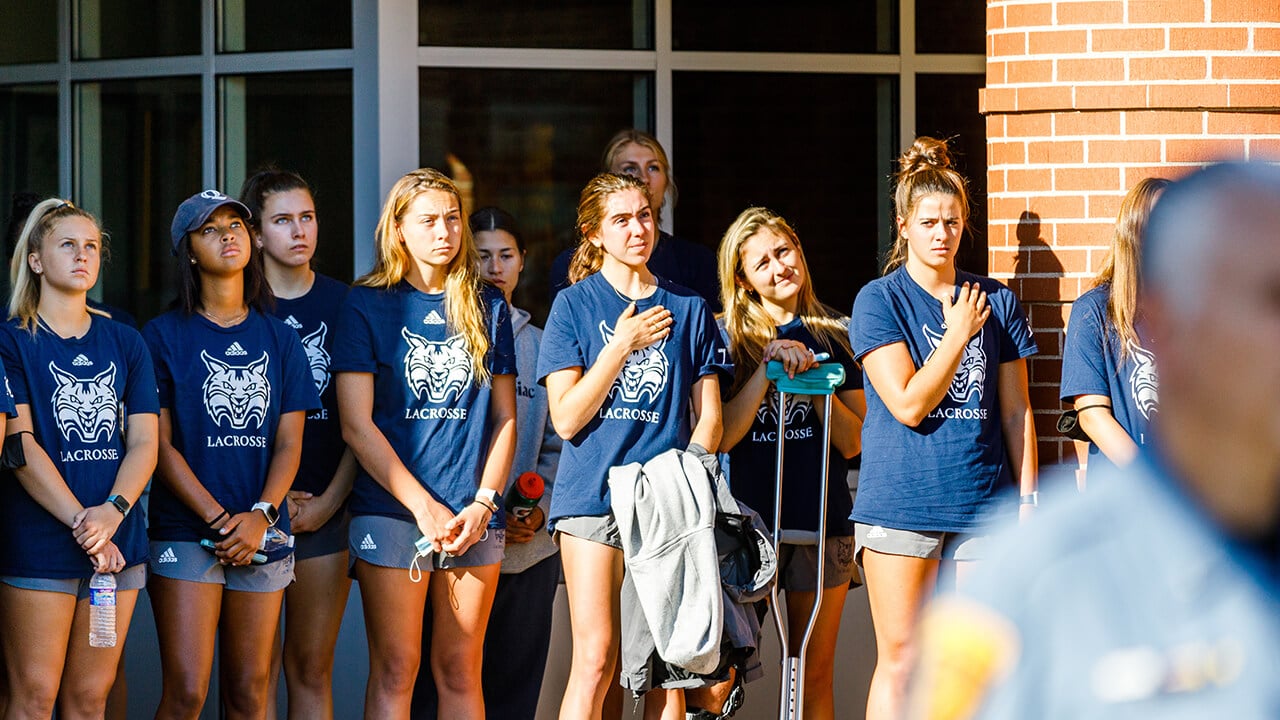 Members of the women's lacrosse team look on during the flag-raising ceremony.