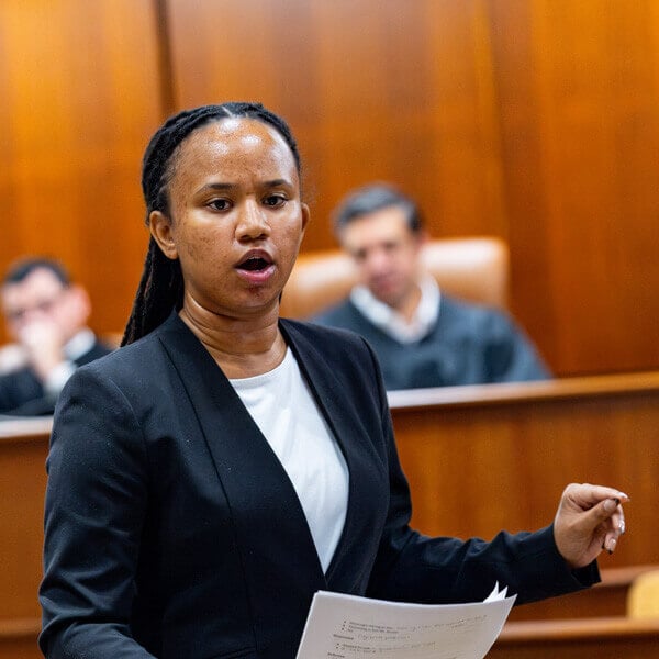A student in a blazer holding a paper as she argues in a courtroom.