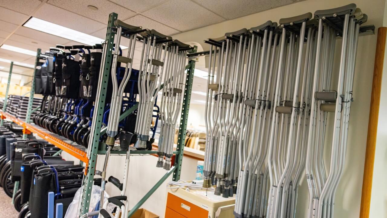 Rows of crutches, wheelchairs, and other mobility aids are neatly organized on storage racks inside an equipment lending facility. The space contains a large inventory of assistive devices available for community use.