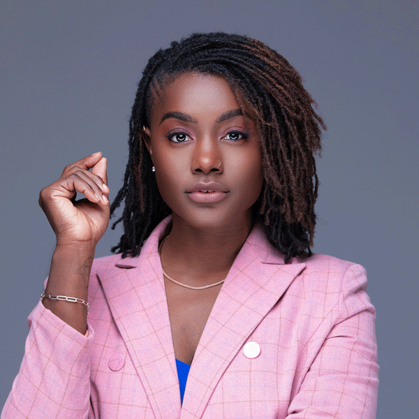 Mercy Quaye in a bright pink formal coat against a grey background