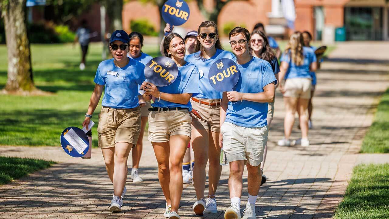 A group of Quinnipiac student tour guides cheer as they walk across the quad during Open House