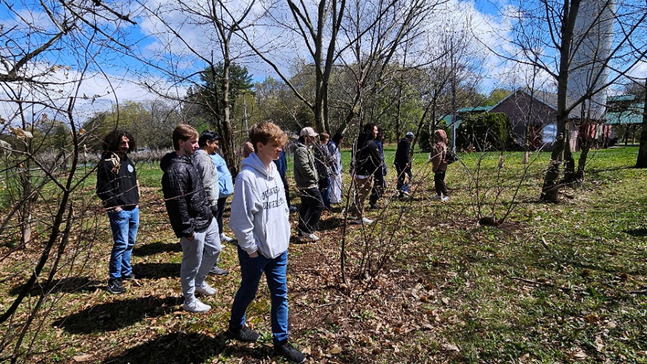 A group of students walking through woods next to a barn and silo.
