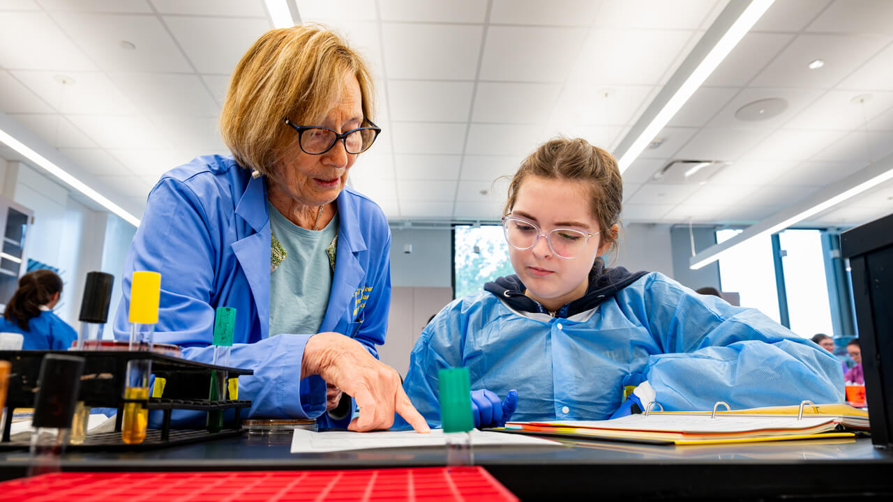 A faculty member pointing at something on a piece of paper in front of a student sitting at a lab table.