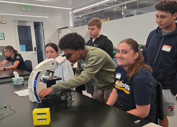 A group of students working around a microscope at a lab table.