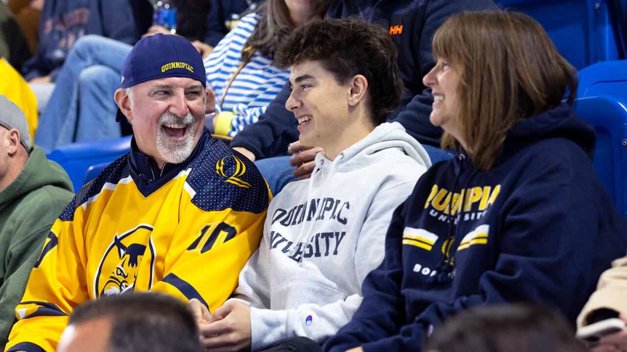 A student and his family sit and laugh together in the seats of the ice hockey arena