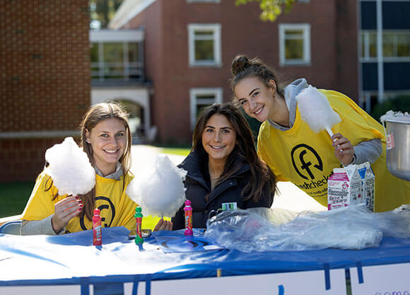 Students sit around table while holding cotton candy and wearing yellow fresh check day shirts.