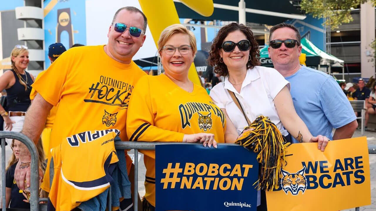 Alumni attend the national hockey championship holding flags and wearing Quinnipiac shirts.