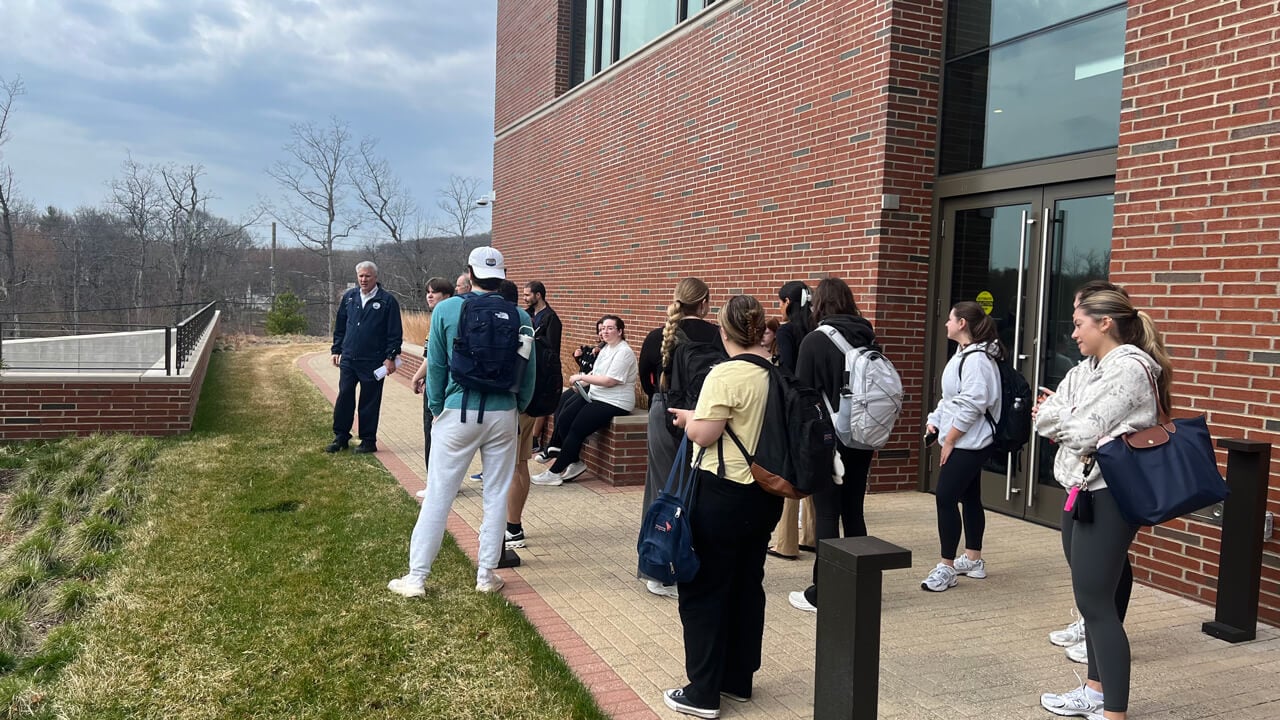The students standing outside The SITE listening to the Facilities expert talk.