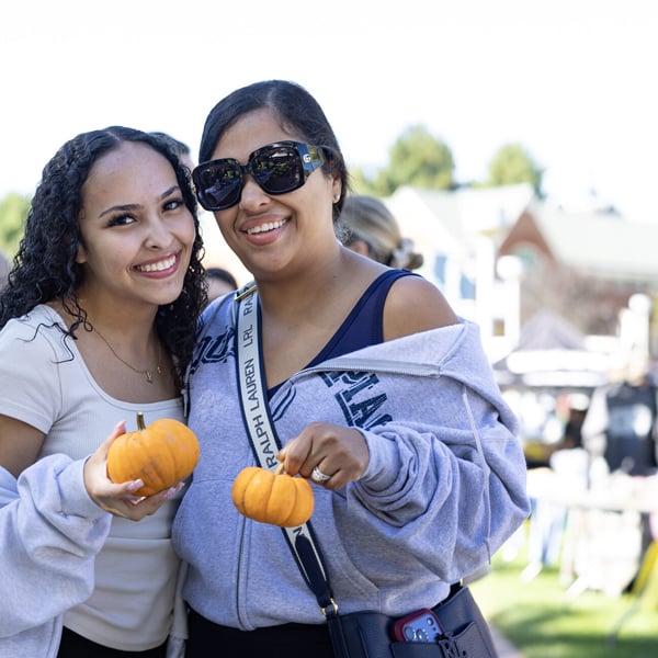 A student and her loved one pose with small pumpkins during Bobcat Weekend