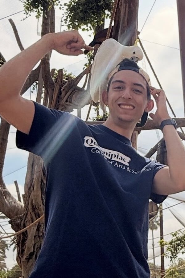 Photo of Younes Benbrahim smiling with a white bird perched on his head.
