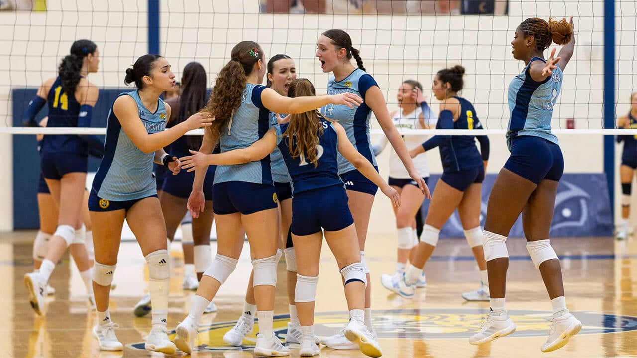 Volleyball players jump and embrace on the court in excitement.