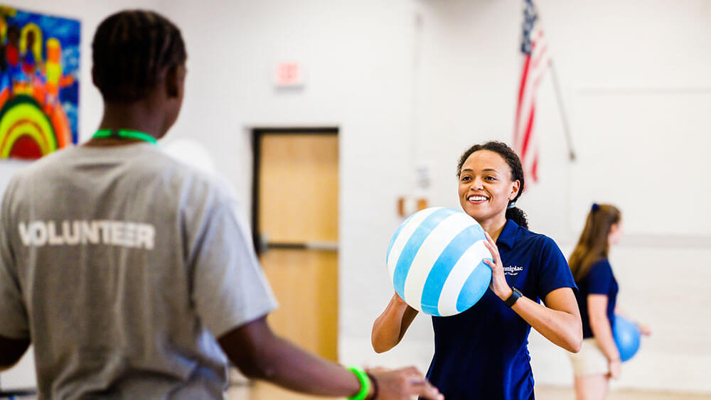 A physical therapy student passes a large ball to a local teen during a physical therapy workshop exercise