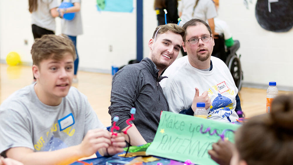 A student smiles next to a local man during an arts and crafts workshop for special needs athletes