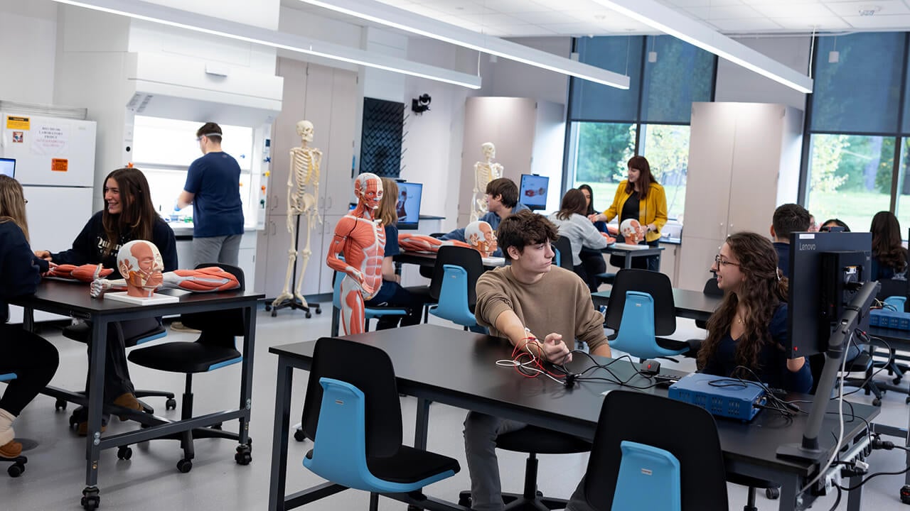 Students participate in hands-on activities at laboratory stations surrounded by anatomical models, skeletons, computers and electronic equipment.