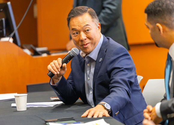 Symposium panelist talking into a microphone while placing his hand on the table
