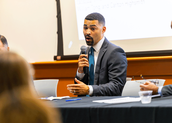 Individual talking into a microphone to the crowd at the School of Law symposium