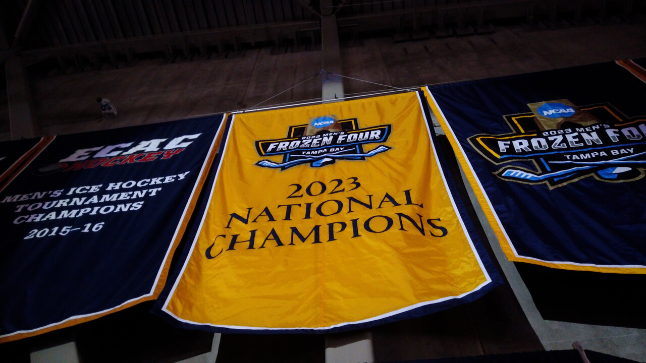 2023 men's ice hockey national championship banner rises under a spotlight in the Quinnipiac arena