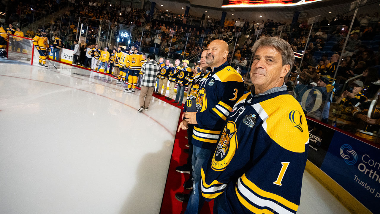 Hockey alumni stand on the ice during the banner raising