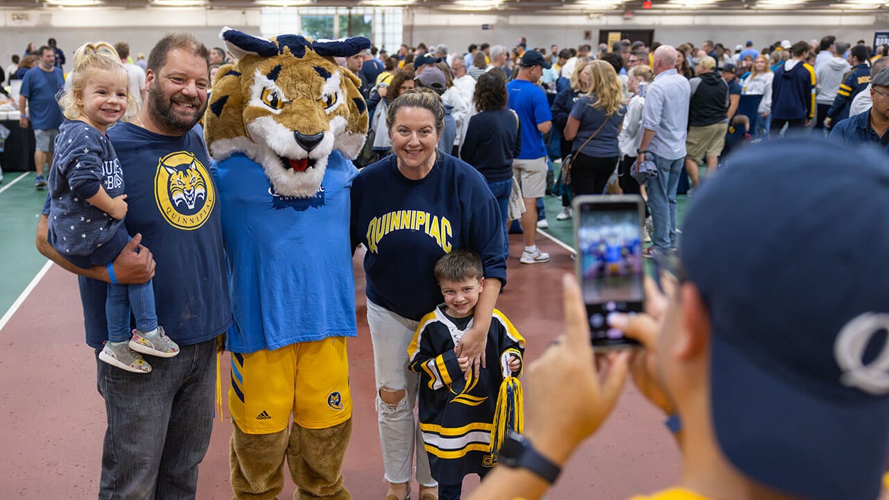 A family decked out in Quinnipiac spirit wear smiles with Boomer the bobcat