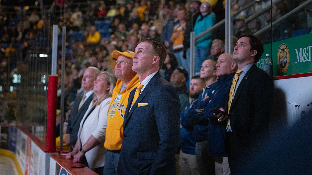 Men's Ice Hockey Coach Rand Pecknold stands with the team on the ice