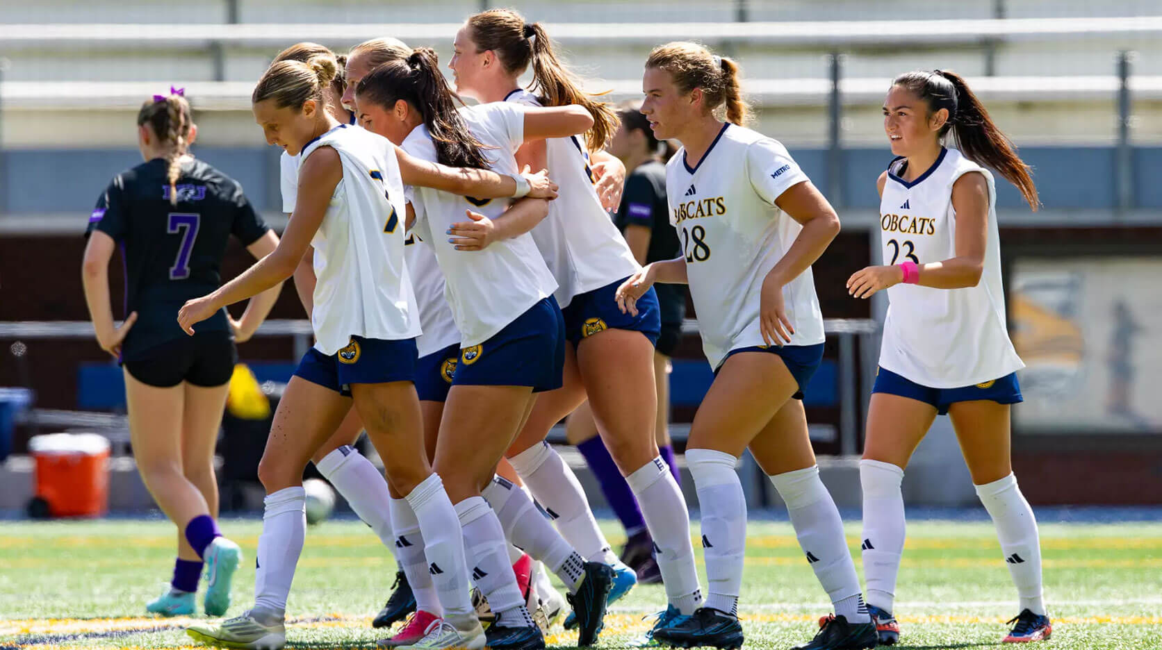 Members of the women's soccer team embrace on the field as they walk forward.